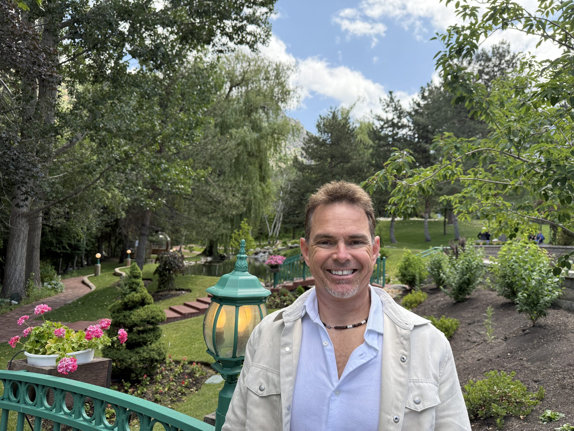 Pete smiling on a green garden bridge with mountains behind